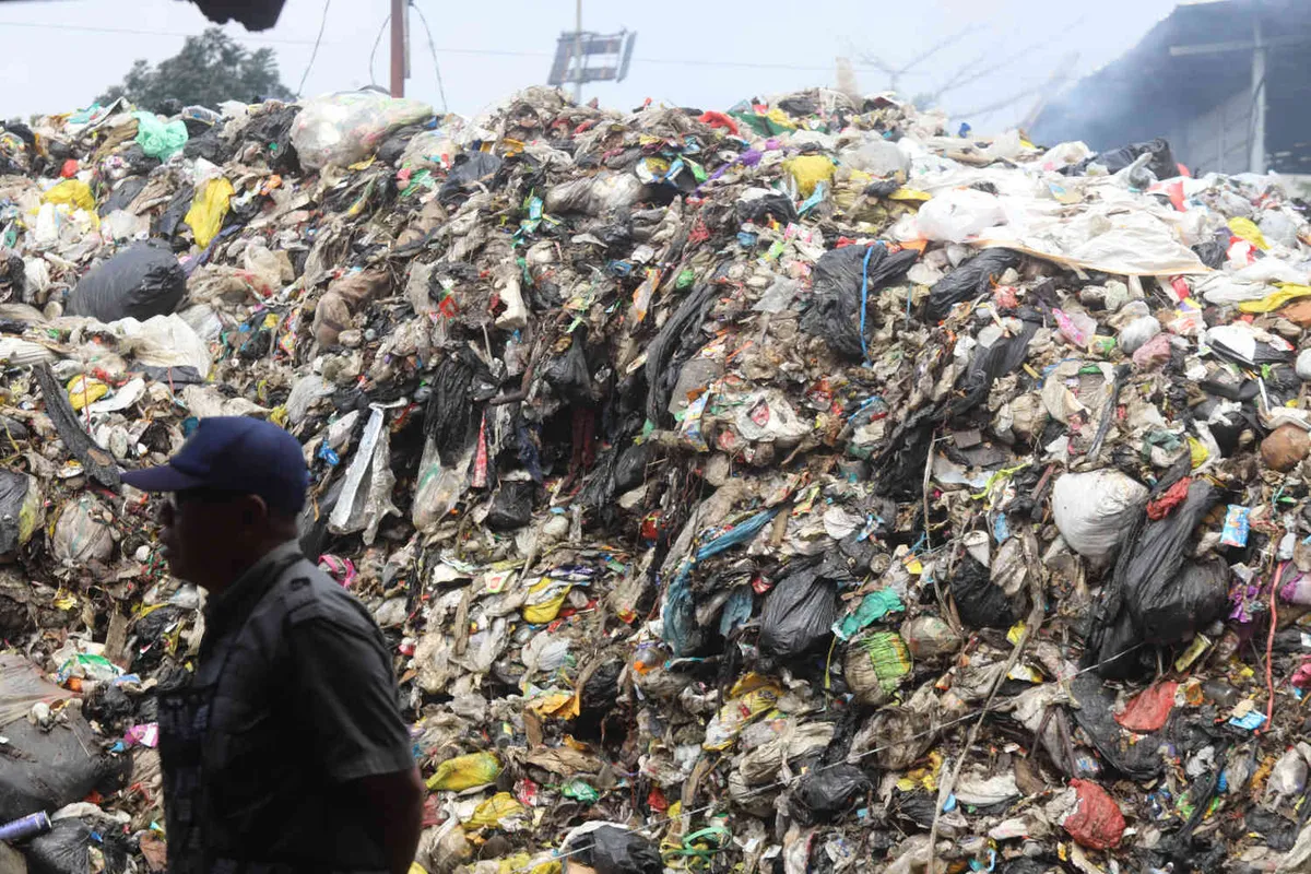 Warga melintas di depan tumpukan sampah di TPS Pasar Ciwastra, Kota Bandung, Selasa 22 April 2025. Penumpukan tejadi diakibatkan pembatasan pembuangan sampah ke TPA Sarimukti. (Sumber: ayobandung.id | Foto: Irfan Al Faritsi)