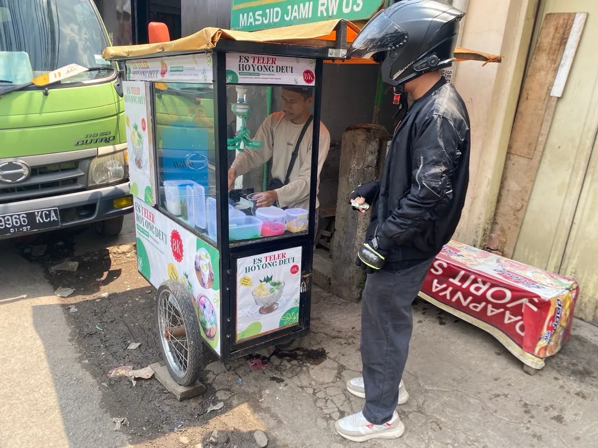 Penjual melayani pembeli yang berenti di depan gerobaknya dikawasan Caringin pada siang hari 1-12-2025 (Sumber: Raifan Firdaus Al Farghani | Foto: Raifan Firdaus Al Farghani)