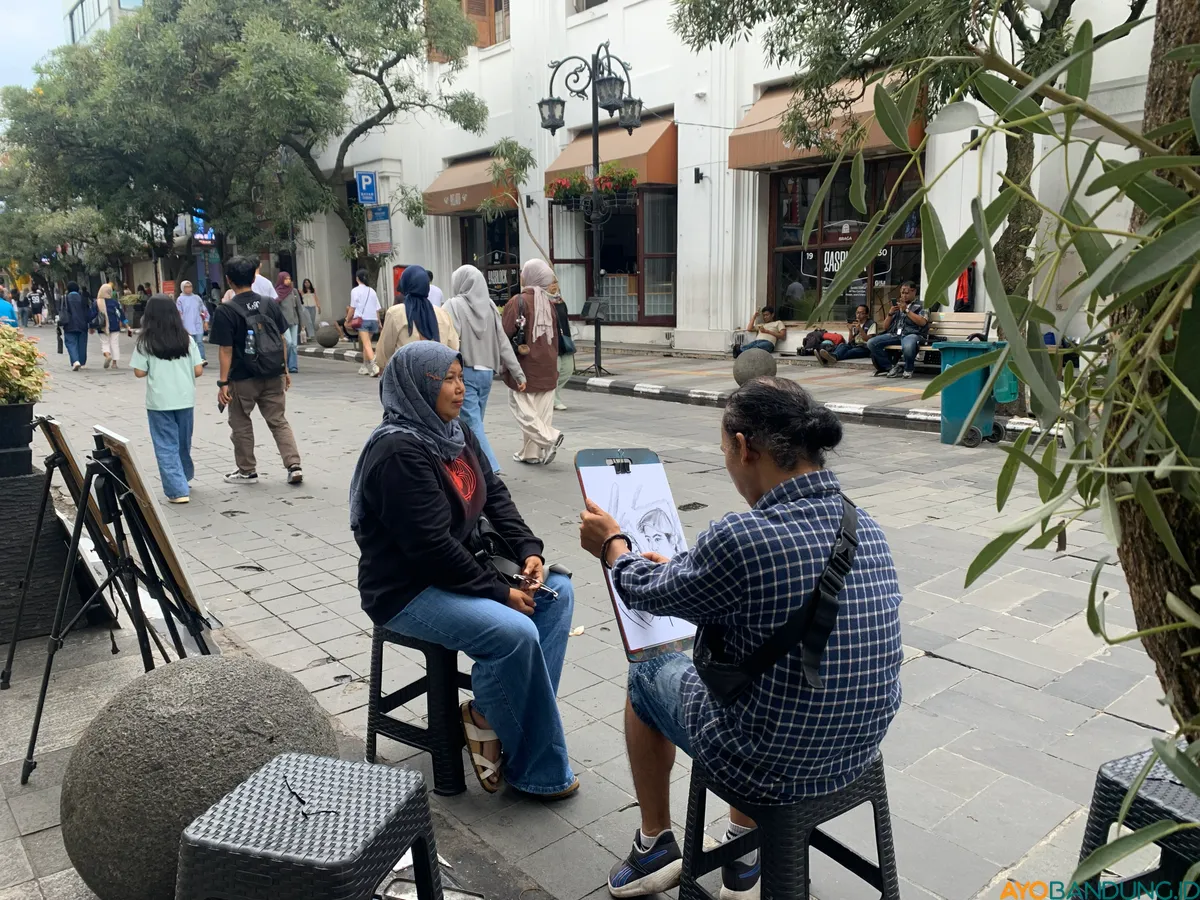 Seorang pelukis di Jalan Braga sedang mengerjakan pesanan dari seorang wisatawan lokal. (Sumber: ayobandung.id | Foto: Toni Hermawan)