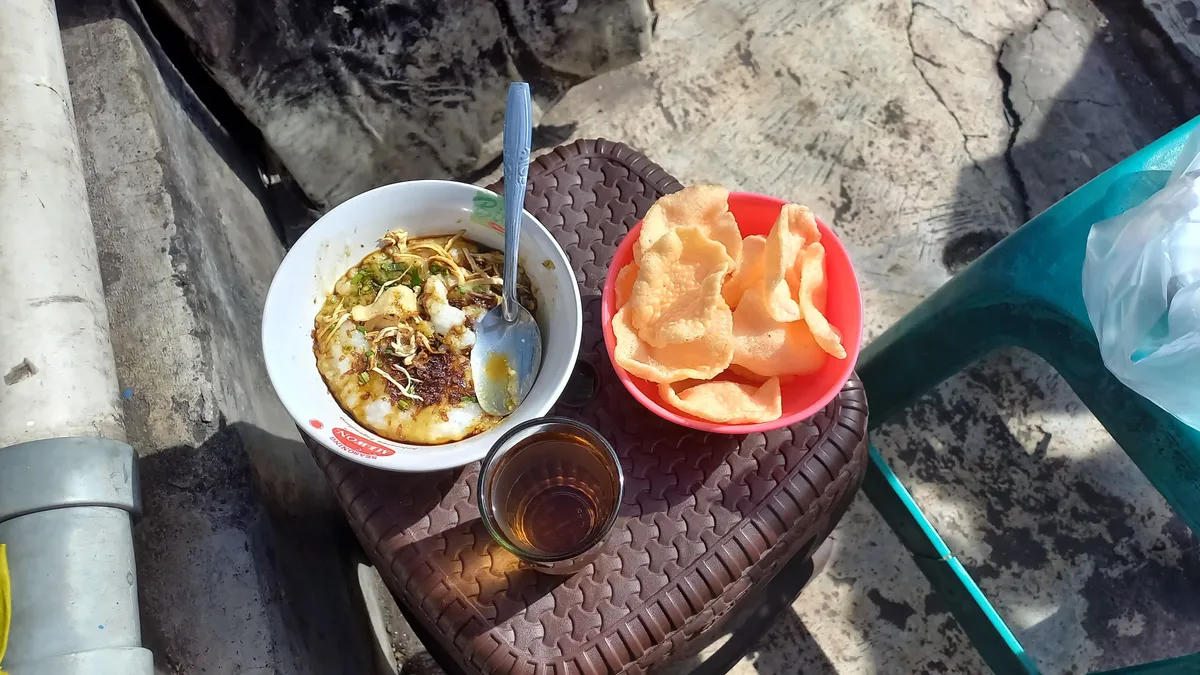 Tampilan semangkuk bubur ayam Mang Opik yang ditemani toppingnya dengan semangkuk krupuk dan teh hangat (Sumber: Dokumentasi Pribadi Penulis | Foto: Salsabiil Firdaus)