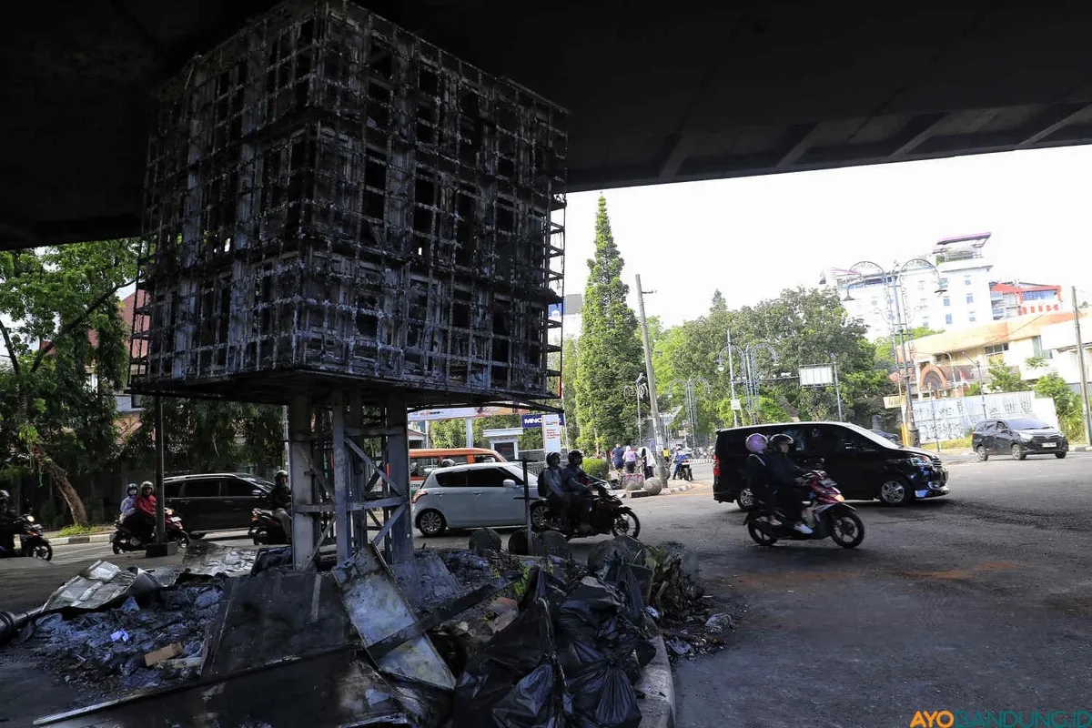 Warga melintas didekat videotron dan pos polisi yang dibakar massa unjukrasa pada Jumat 29 Agustus 2025 di Kawasan Cikapayang, Jalan Ir H. Djuanda, Kota Bandung, Sabtu 30 Agustus 2025. (Sumber: ayobandung.id | Foto: Irfan Al- Faritsi)