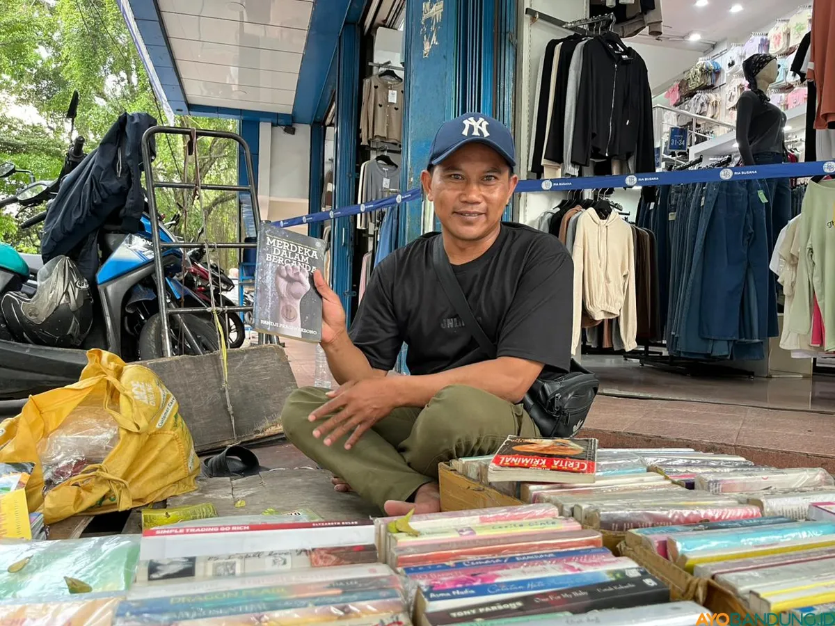 Wawan menunjukkan buku Merdeka dalam Bercanda yang ditulis Pandji Pragiwaksono dan pernah menjadi buruan peminat Stand-Up Comedy saat booming di tahun 2011. (Sumber: ayobandung.id | Foto: Ilham Maulana)
