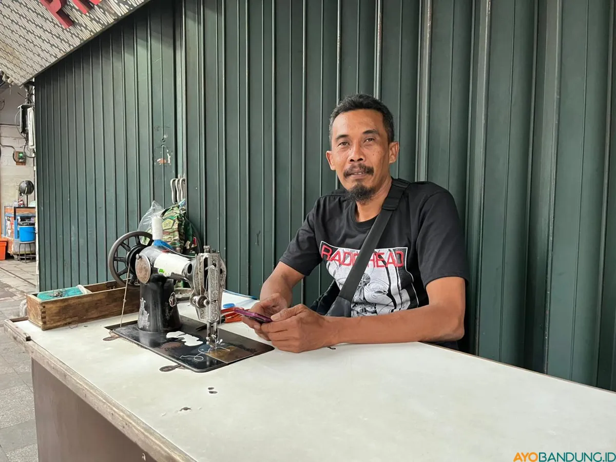 Andi tetap menjahit di tengah sepinya pelanggan, mengandalkan keahlian yang ia pelajari secara otodidak. (Sumber: ayobandung.id | Foto: Ilham Maulana)
