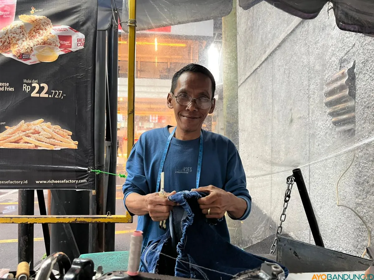 Ade Gares setia menjaga lapak jahitnya sejak 1994, bertahan di tengah perubahan zaman dan kondisi ekonomi. (Sumber: ayobandung.id | Foto: Ilham Maulana)