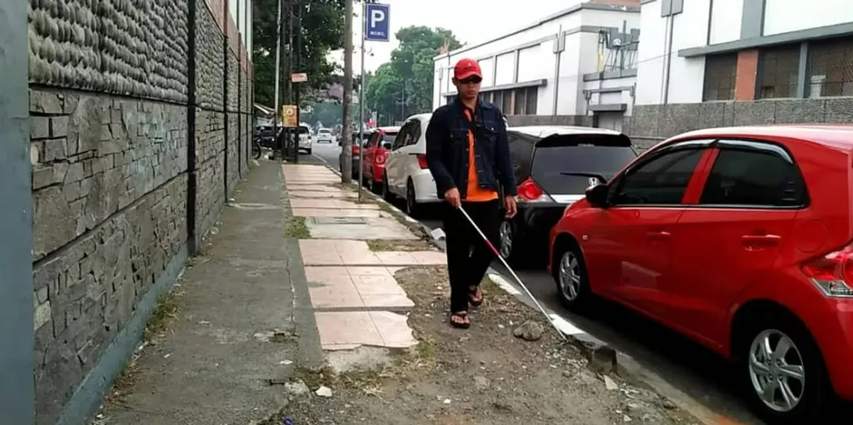 Seorang penyandang disabilitas netra berjalan di atas trotoar yang rusak di Jalan Cicendo, Kota Bandung. (Sumber: Ayobandung.com | Foto: Eneng Reni Nuraisyah Jamil)