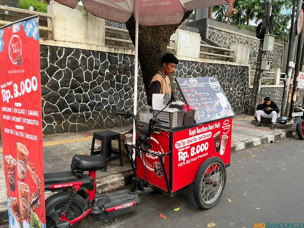 Fandi Ginanjar sedang meracik pesanan pelanggan di gerobak sepeda listrik Tony’s Coffee saat mangkal di kawasan kampus Jalan Tamansari, Bandung. (Sumber: ayobandung.id | Foto: Ilham Maulana)