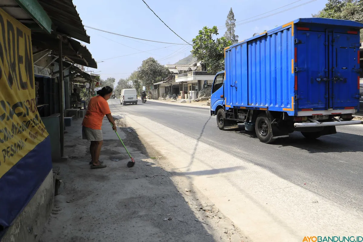 Seorang ibu menyapu debu yang mengendap di halaman rumahnya akibat aktivitas pengolahan batu gamping di sekitar permukiman. (Sumber: ayobandung.id | Foto: Irfan Al Faritsi)