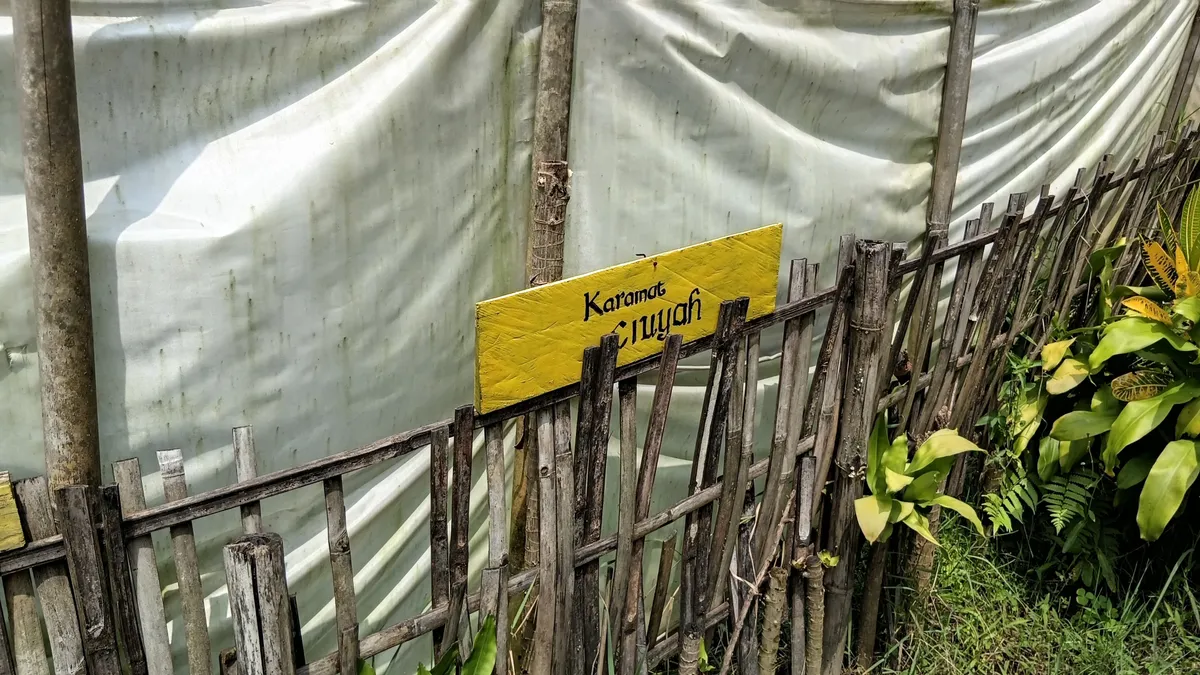 Papan penanda kayu bertuliskan "Karamat Ciuyah" yang terpasang di pagar bambu sekitar lokasi mata air asin di Desa Ciuyah, Kabupaten Sumedang. (Sumber: Dokumentasi Pribadi | Foto: Fatia Siti Biladi)