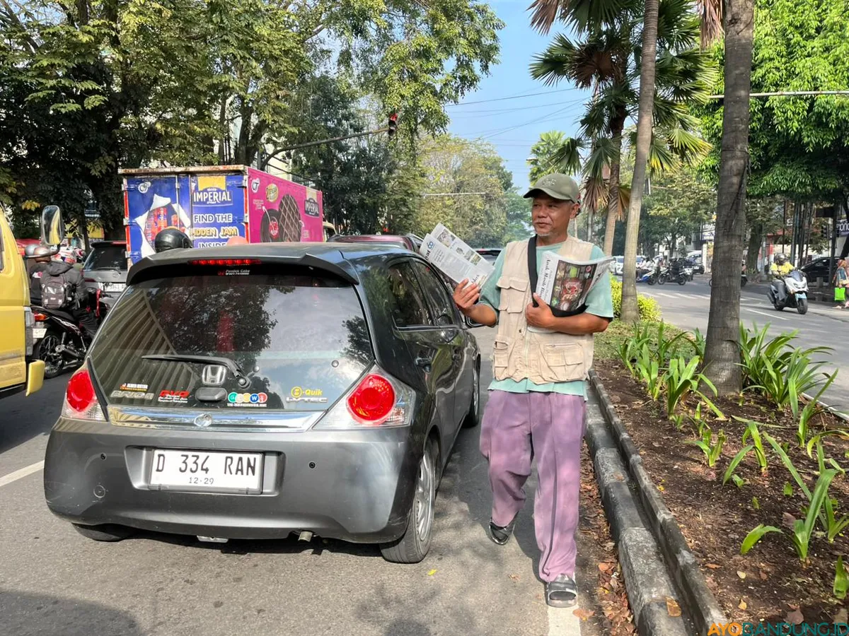 Iyan menyusuri antrean kendaraan di persimpangan Jalan BKR, menawarkan koran yang pembelinya tinggal hitungan jari. (Sumber: ayobandung.id | Foto: Ilham Maulana)