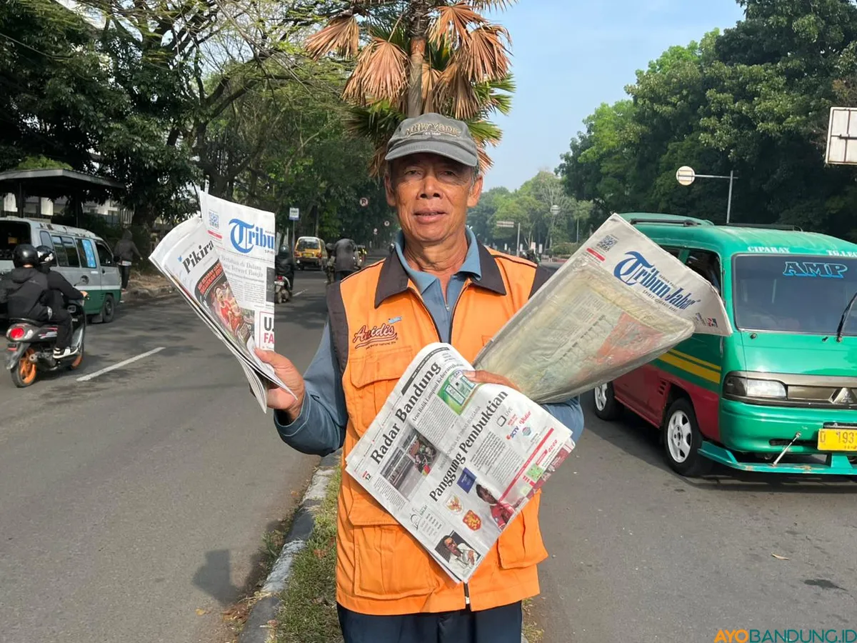 Sutisna berdiri di bawah terik matahari di lampu merah Tegalega, menunggu pembelinya yang semakin jarang. (Sumber: ayobandung.id | Foto: Ilham Maulana)
