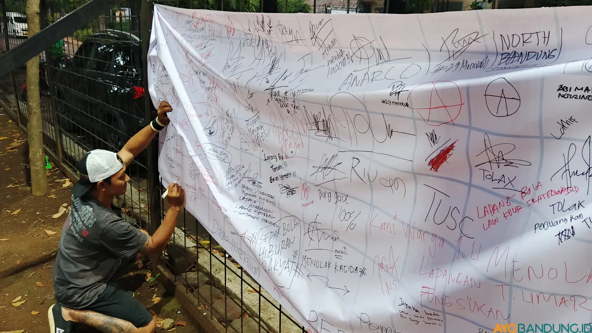 Seorang warga menuliskan pesan dan membubuhkan tanda tangan pada kain spanduk sebagai bentuk dukungan terhadap penolakan rencana revitalisasi Lapangan Teuku Umar, Coblong, Kota Bandung. (Sumber: ayobandung.id | Foto: Gilang Fathun Romadhan)