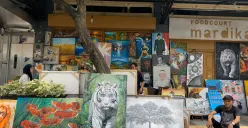 Ian seorang pelukis lokal dan karya lukisannya yang dipajang di trotoar Jalan Braga. (Sumber: ayobandung.id | Foto: Toni Hermawan)