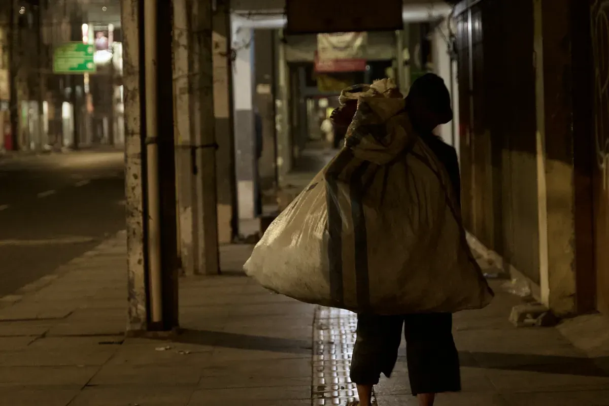 Seorang tunawisma menyusuri lorong Pasar pada malam hari (29/10/25) dengan memanggul karung besar di Jln. ABC, Braga, Sumur Bandung, Kota Bandung. (Foto: Rajwaa Munggarana)