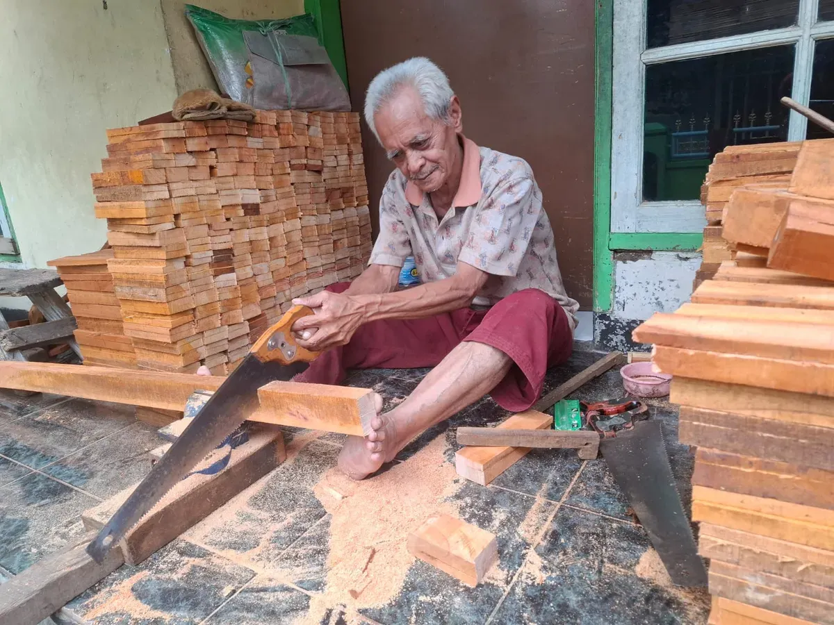 Abah Alek memotong papan kayu menggunakan gergaji tangan, proses awal pembuatan sikat. (Foto: Lamya Fatimatuzzahro)