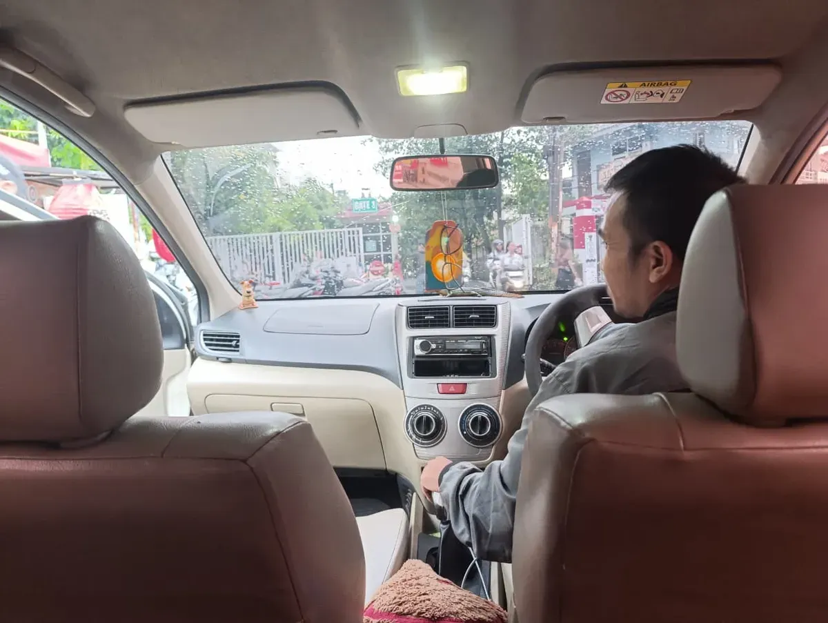 Seorang driver online tengah tersenyum ramah menunggu penumpangnya di tengah keramaian jalanan, menerapkan nilai cageur, bager, bener dalam layanan transportasi – Bandung, Sabtu (01/11/2025) (Foto: Bunga Kemuning A.D)