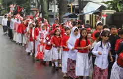 Sejumlah siswa SD Negeri 067 Nilem dengan didampingi guru dan orang tua mengikuti karnaval merah putih saat melintas di Jalan Nilem, Kota Bandung, Kamia 14 Aguatus 2025. (Sumber: Ayobandung.id | Foto: Irfan Al-Faritsi)
