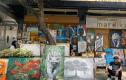 Ian seorang pelukis lokal dan karya lukisannya yang dipajang di trotoar Jalan Braga. (Sumber: ayobandung.id | Foto: Toni Hermawan)