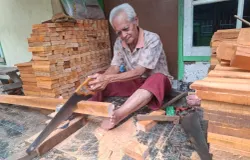 Abah Alek memotong papan kayu menggunakan gergaji tangan, proses awal pembuatan sikat. (Foto: Lamya Fatimatuzzahro)