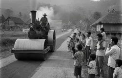 Ilustrasi stum yang sedang meratakan jalan di tahun 1980 an disaksikan masyarakat sekitar. (Sumber: Gemini AI)