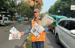 Loper koran tetap berjalan menyusuri antrean kendaraan, meski kini orang terbiasa mencari informasi lewat ponsel. (Sumber: ayobandung.id | Foto: Ilham Maulana)