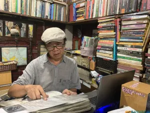 Pendiri Perpustakaan Batu Api, Anton Solihin, duduk di tengah tumpukan buku koleksi pribadinya. (Sumber: ayobandung.id | Foto: Halwa Raudhatul)