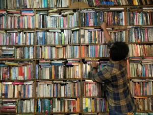 Seorang pengunjung mencari buku di antara rak-rak sempit Perpustakaan Batu Api, Jatinangor, Sabtu 9 Mei 2026. (Sumber: ayobandung.id | Foto: Halwa Raudhatul)