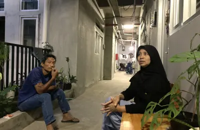 Wawan (duduk) di lorong rumah deret Tamansari, ia berusaha bertahan dengan pekerjaan serabutan di tengah perubahan hidup pascarelokasi. (Sumber: ayobandung.id | Foto: Halwa Raudhatul)
