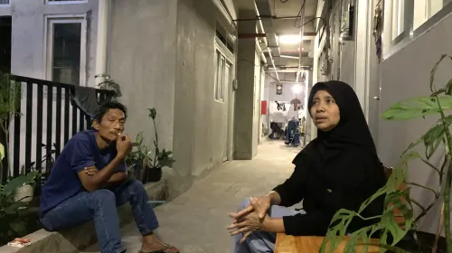 Wawan (duduk) di lorong rumah deret Tamansari, ia berusaha bertahan dengan pekerjaan serabutan di tengah perubahan hidup pascarelokasi. (Sumber: ayobandung.id | Foto: Halwa Raudhatul)