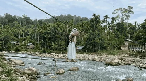 Seorang anak sekolah di Aceh yang menyebrangi jembatan tali menuju sekolah. (Sumber: Generated AI (Terinspirasi dari Video Asli di Aceh))