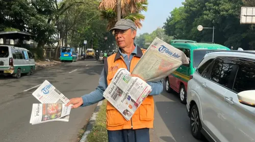 Loper koran tetap berjalan menyusuri antrean kendaraan, meski kini orang terbiasa mencari informasi lewat ponsel. (Sumber: ayobandung.id | Foto: Ilham Maulana)