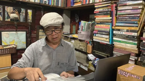 Pendiri Perpustakaan Batu Api, Anton Solihin, duduk di tengah tumpukan buku koleksi pribadinya. (Sumber: ayobandung.id | Foto: Halwa Raudhatul)