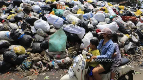 Pengendara melintas di dekat tumpukan sampah yang menggunung di TPS Jalan Makam Caringin, Kota Bandung, Kamis, 9 April 2026. (Sumber: Ayobandung | Foto: Irfan Al-Faritsi)