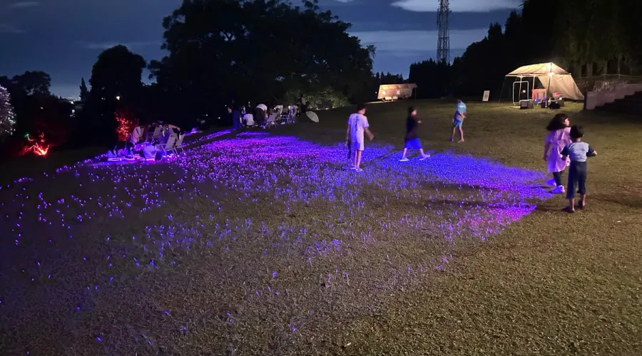 Anak-anak berlarian di atas sorot lampu yang menyapu rumput di Titik Kumpul–Backyard, Bandung, sebagai bagian dari aktivasi seni Sesar Lembang Kalcer dalam menyampaikan literasi mitigasi bencana secara ramah.
