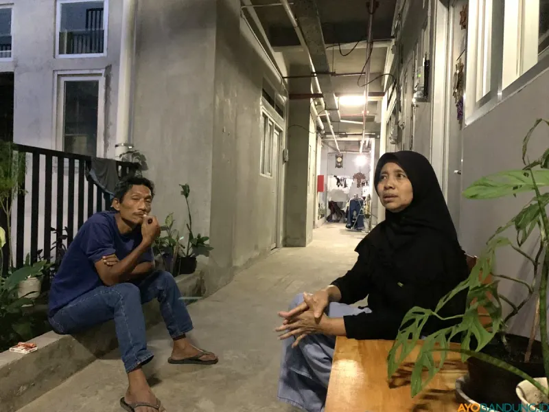 Wawan (duduk) di lorong rumah deret Tamansari, ia berusaha bertahan dengan pekerjaan serabutan di tengah perubahan hidup pascarelokasi. (Sumber: ayobandung.id | Foto: Halwa Raudhatul)