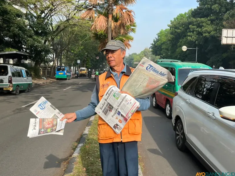 Loper koran tetap berjalan menyusuri antrean kendaraan, meski kini orang terbiasa mencari informasi lewat ponsel. (Sumber: ayobandung.id | Foto: Ilham Maulana)